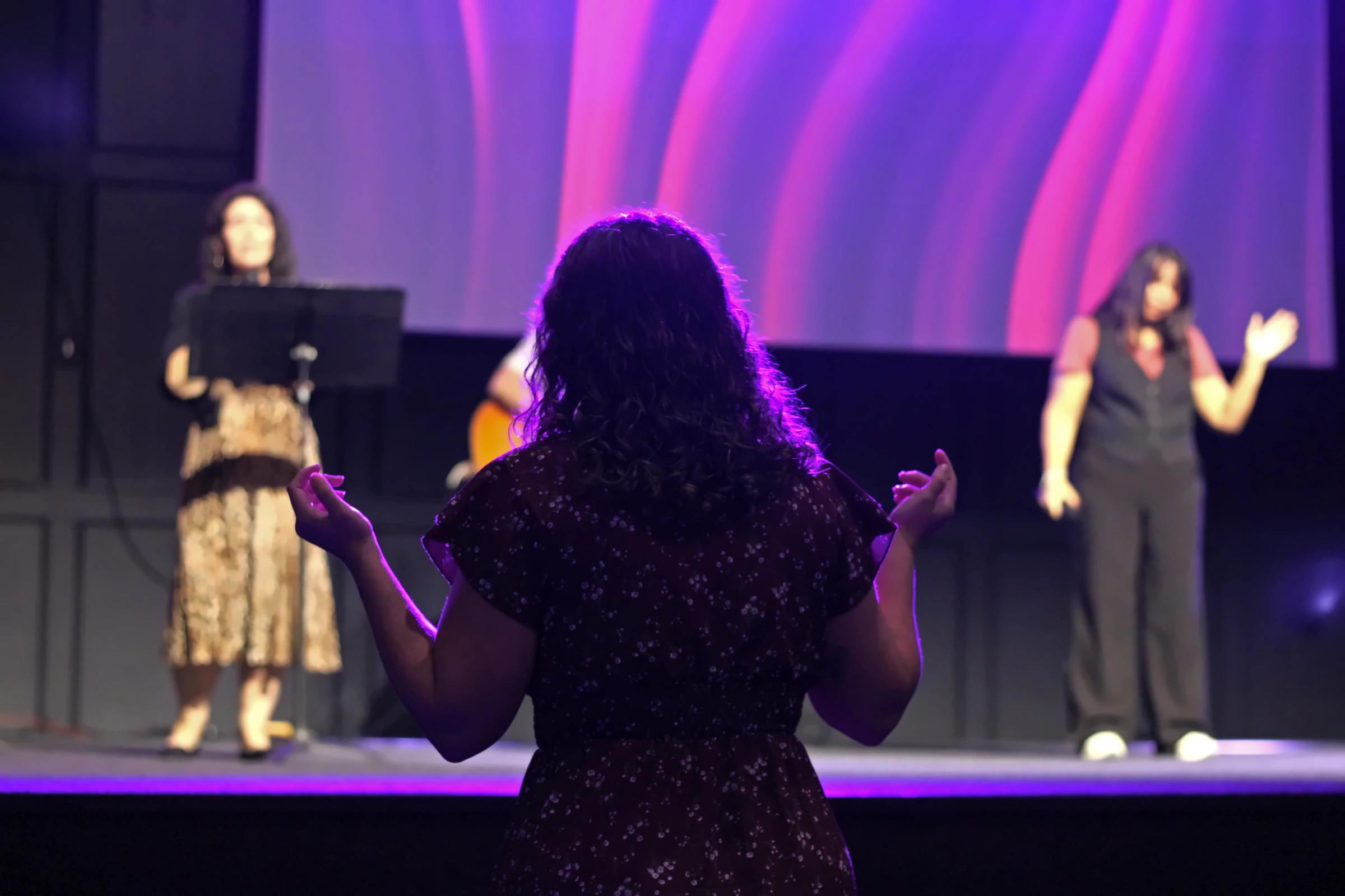 A worshipper faces the singers with open hands in the purple-lit sanctuary.